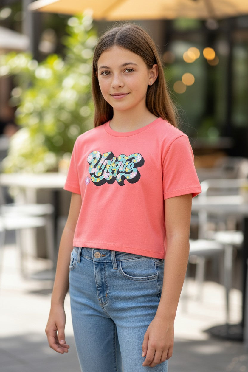 Calla Lily Cosmetics + CL kids coral pink cotton blend crop tee with a retro-style "Unique" graphic featuring flowers and a small pink flower accent.