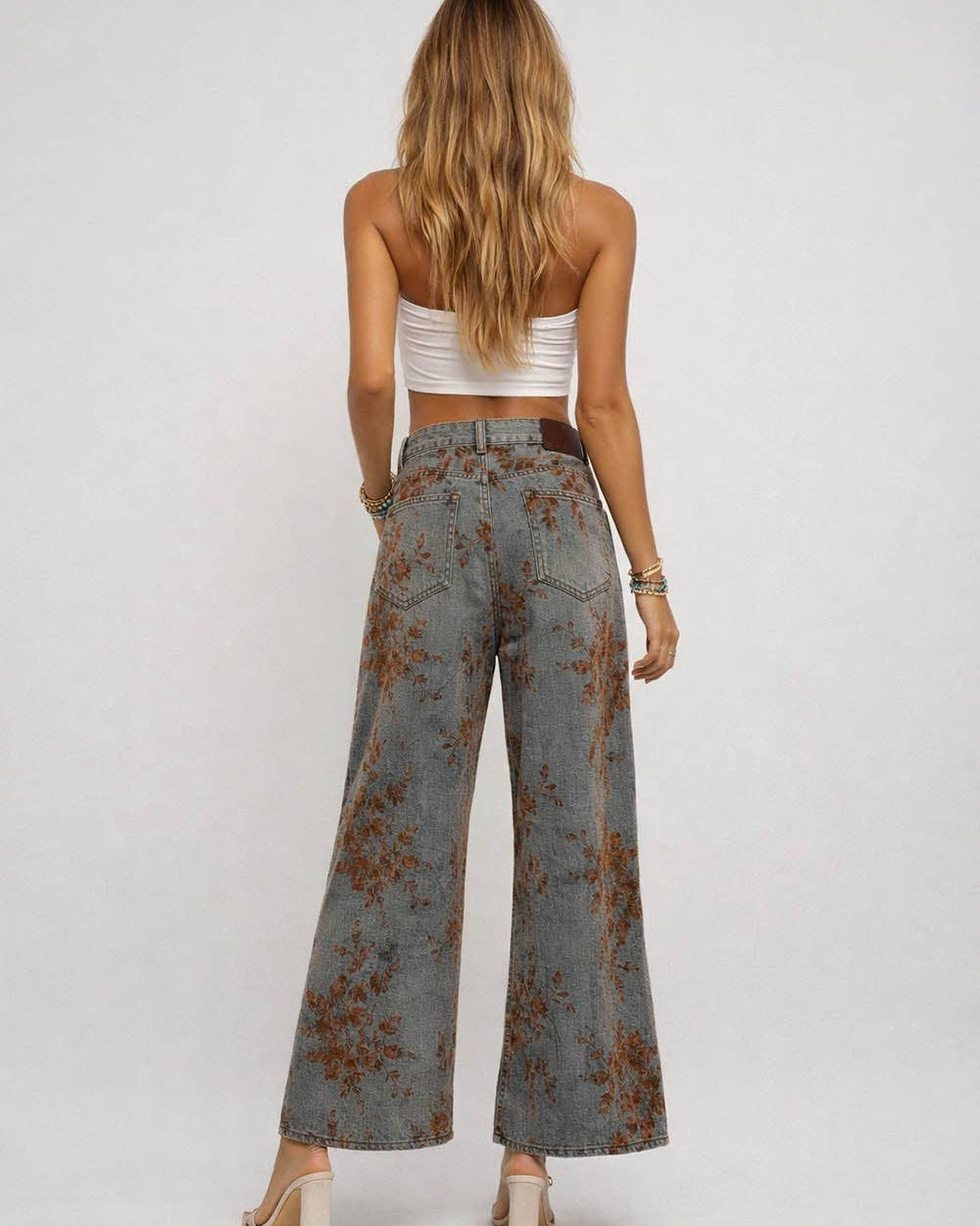 Woman wearing a white top and patterned wide-leg jeans on a plain background