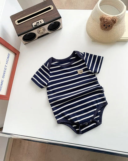 Navy and white striped baby onesie on a white surface with decorative items.