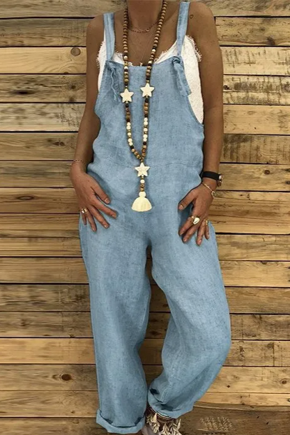 Person wearing light blue denim overalls against a wooden wall.