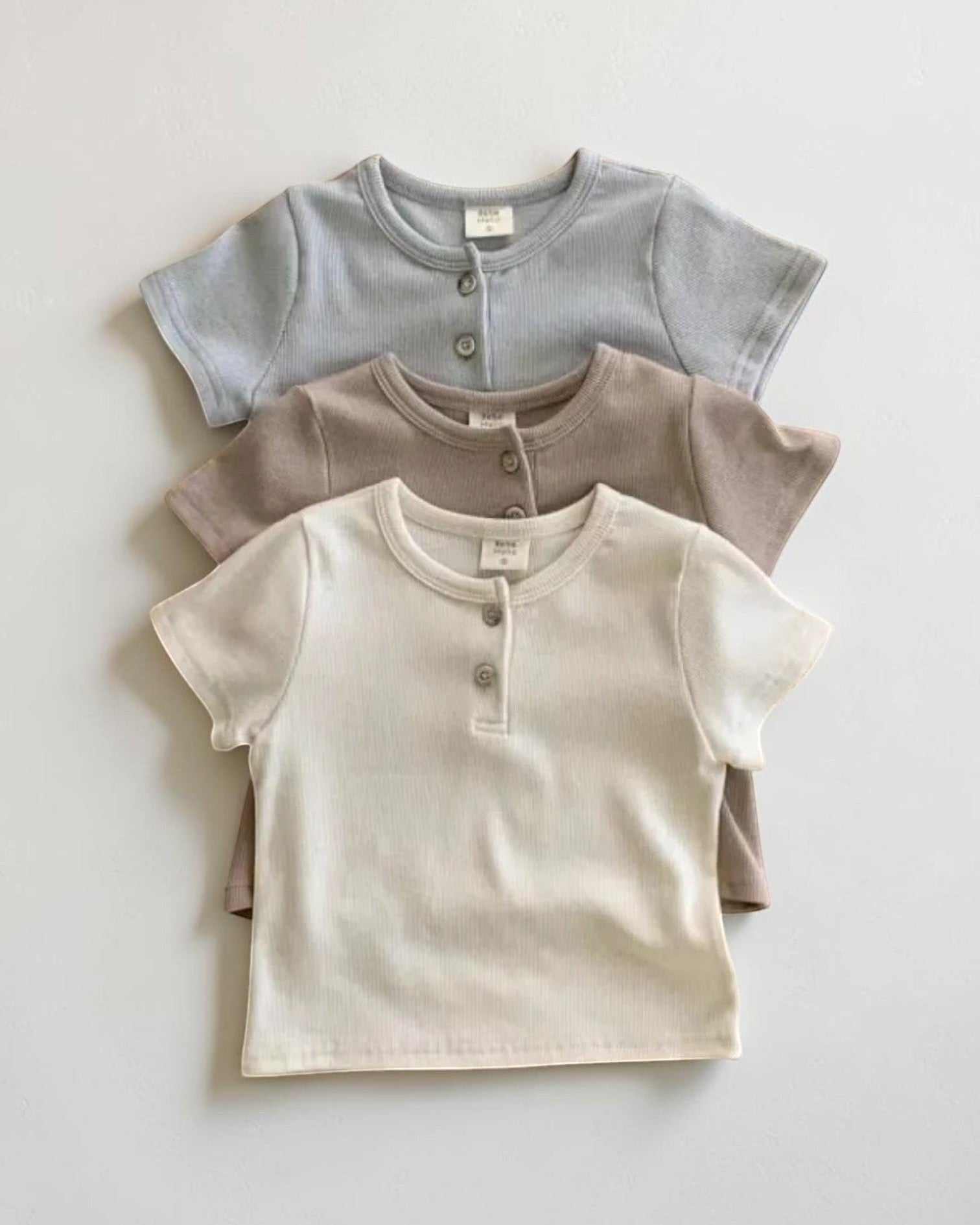 Three children's short-sleeve shirts in gray, beige, and brown on a light gray background.