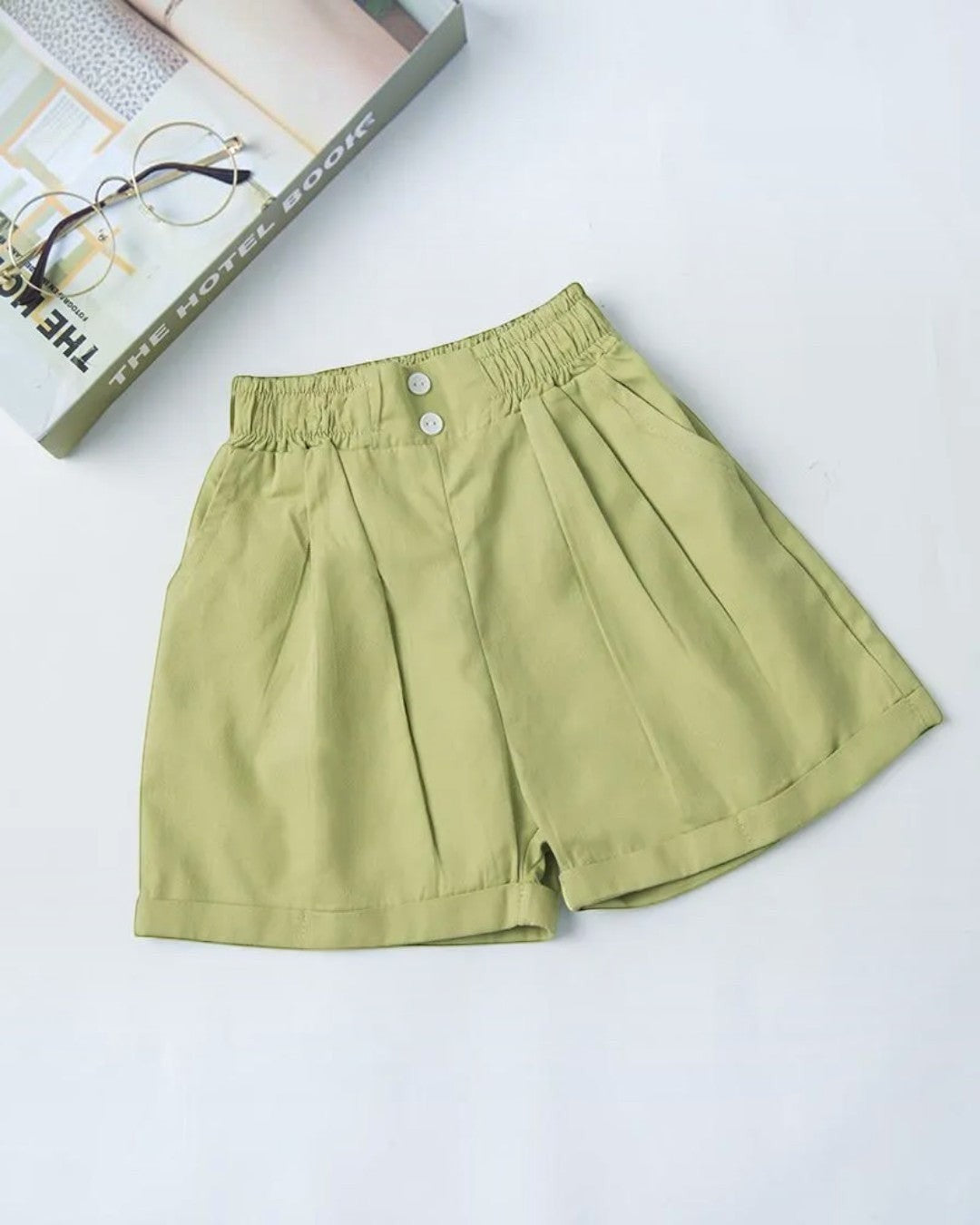 Light green shorts on a white background with a book and glasses in the corner.