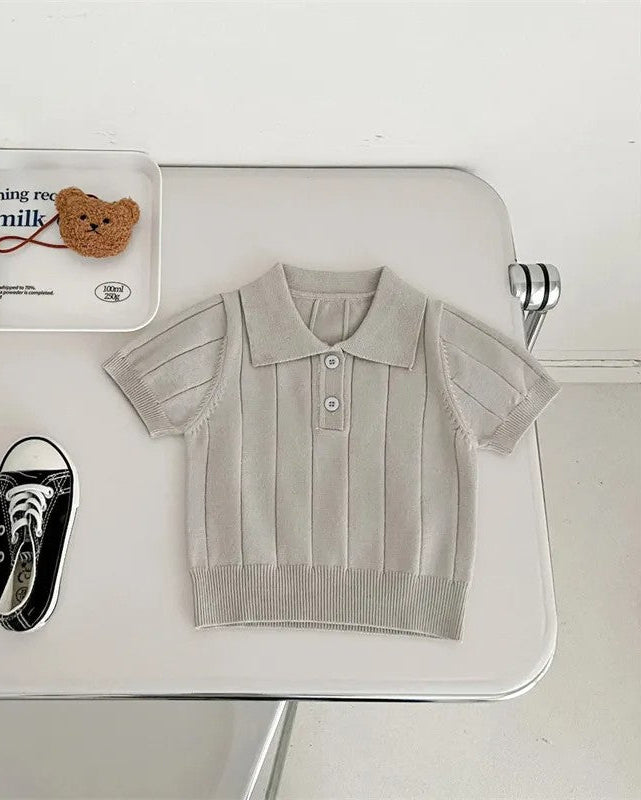 Light gray polo shirt on a white surface with black sneakers and a small bottle.