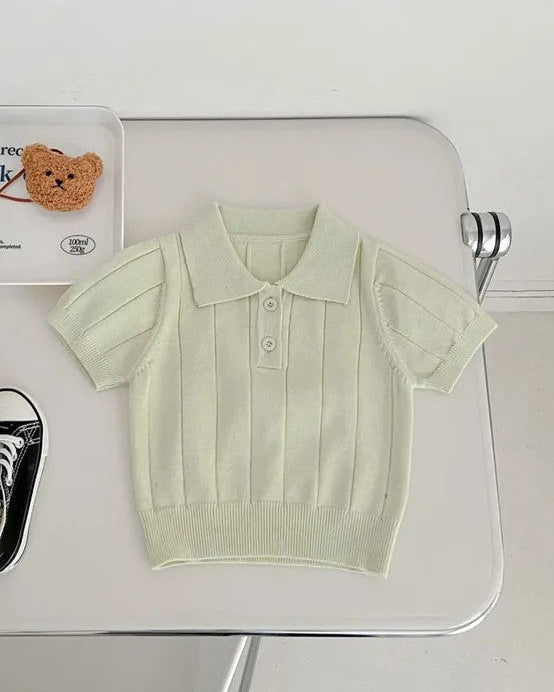 Light green polo shirt, black sneakers, and a small teddy bear on a white surface.