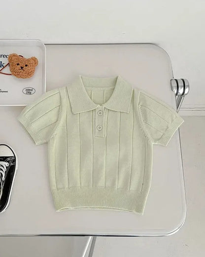 Light green polo shirt, black sneakers, and a small teddy bear on a white surface.