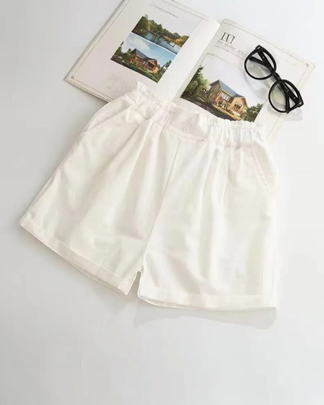 White shorts on a light gray background with a pair of sunglasses and a photo frame.