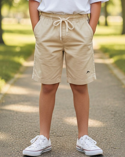 Young person wearing a white t-shirt and beige shorts standing on a path with trees in the background