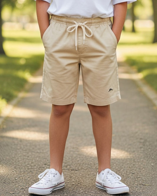 Young person wearing a white t-shirt and beige shorts standing on a path with trees in the background