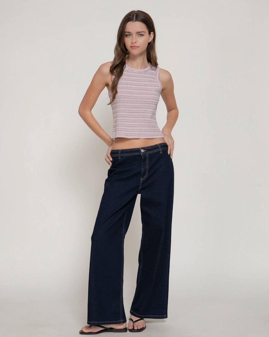 Woman wearing a striped crop top and wide-leg jeans on a plain background