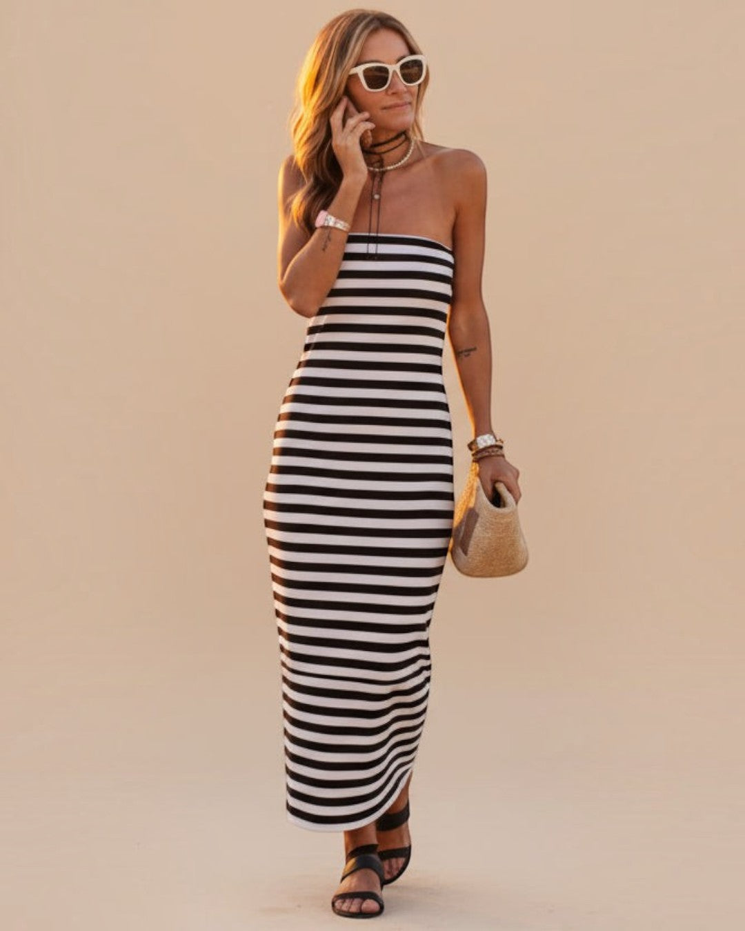 Woman in a black and white striped dress leaning against a table outdoors.
