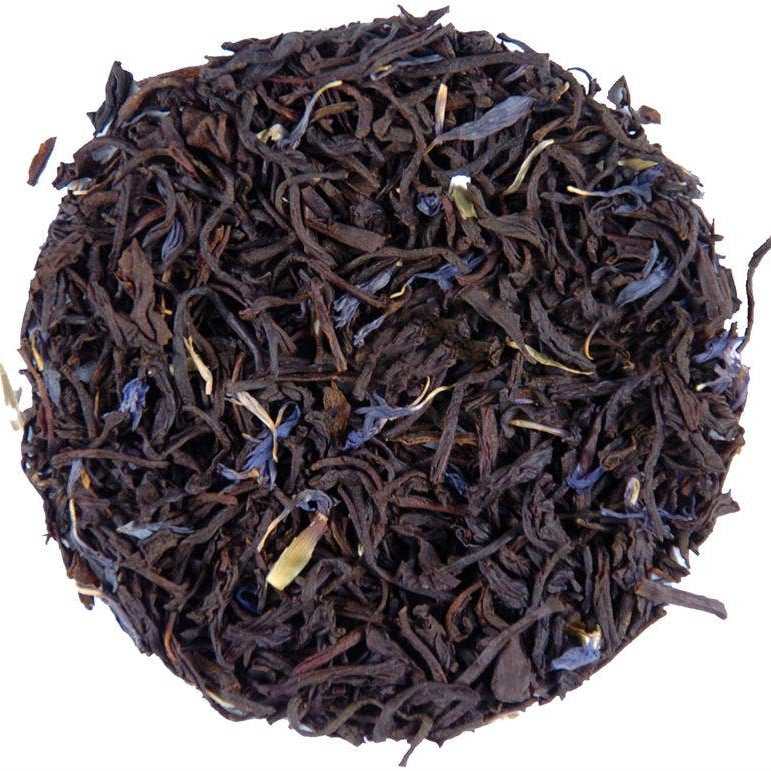 A circular pile of dark brown loose-leaf tea with scattered small blue-purple flower buds and a few pale yellow-green tips, photographed on a plain white background.