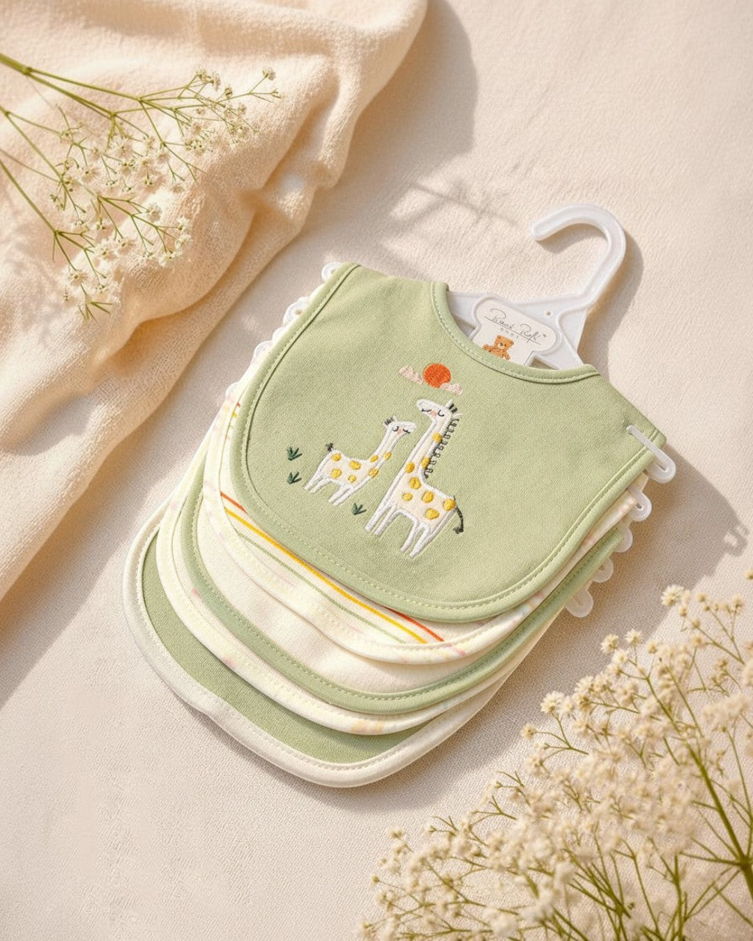 Stack of green baby bibs with giraffe design on a beige background
