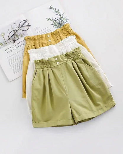 Two pairs of shorts, one yellow and one green, on a white surface with a magazine and glasses in the background.