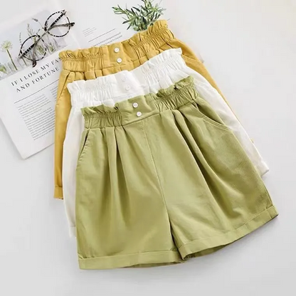 Two pairs of shorts, one yellow and one green, on a white surface with a magazine and glasses in the background.