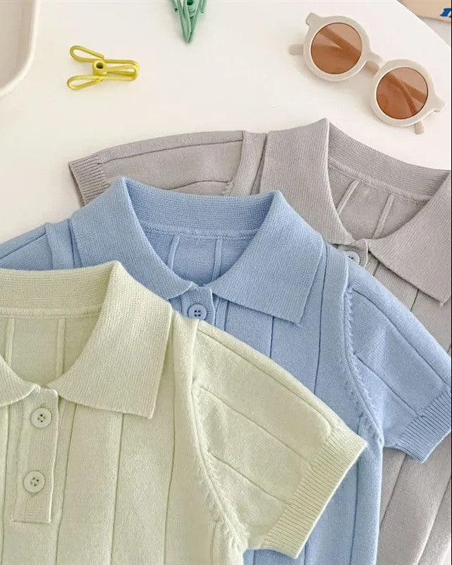 Three polo shirts in green, blue, and gray on a white surface with a plate and sunglasses.