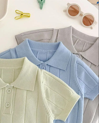 Three polo shirts in green, blue, and gray on a white surface with a plate and sunglasses.