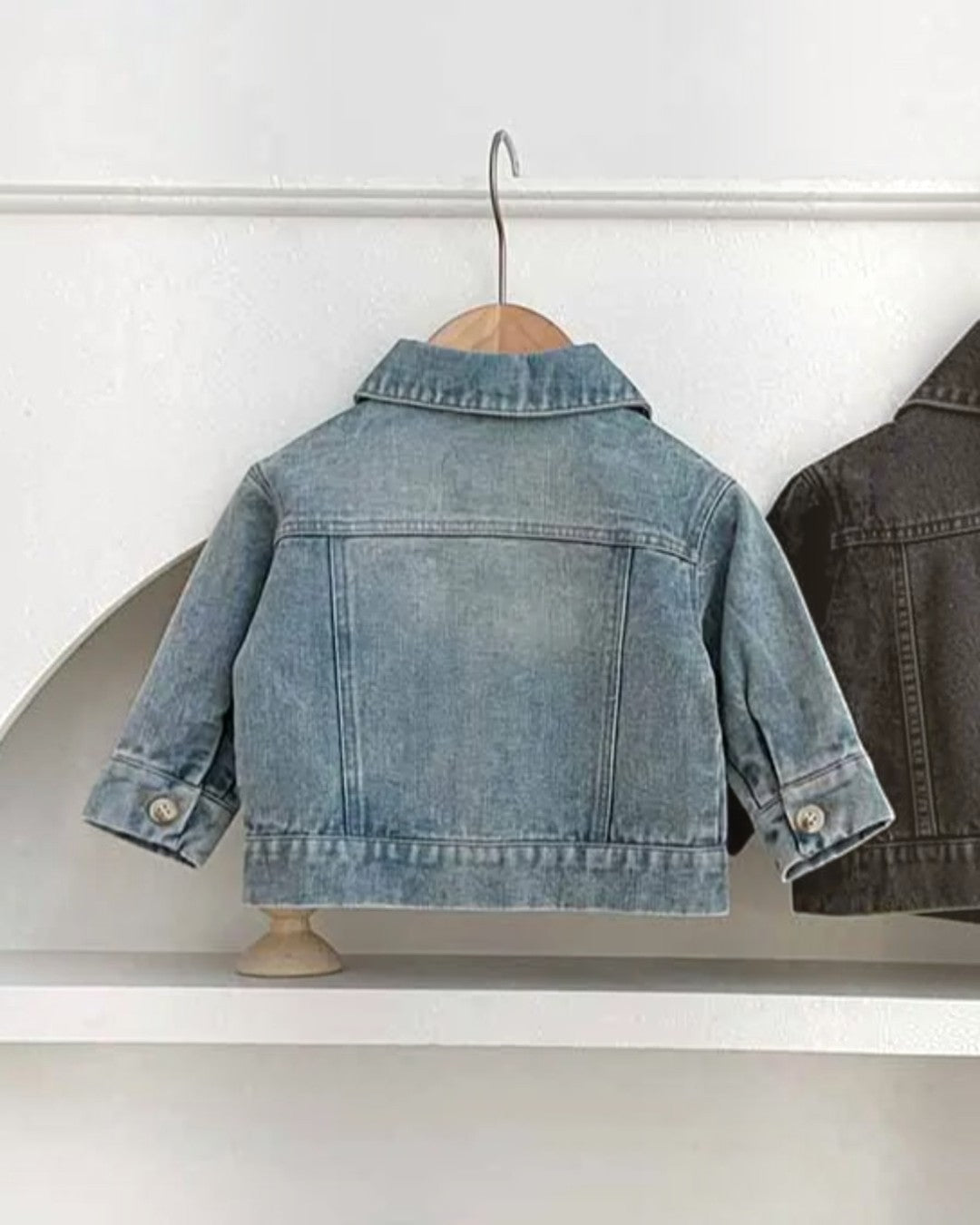 Two denim jackets, one blue and one black, on hangers against a white background.