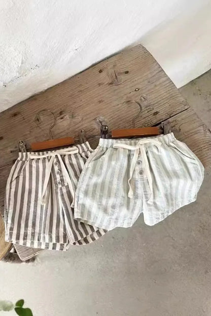 Two pairs of shorts hanging on a wooden board with a plant in the background.
