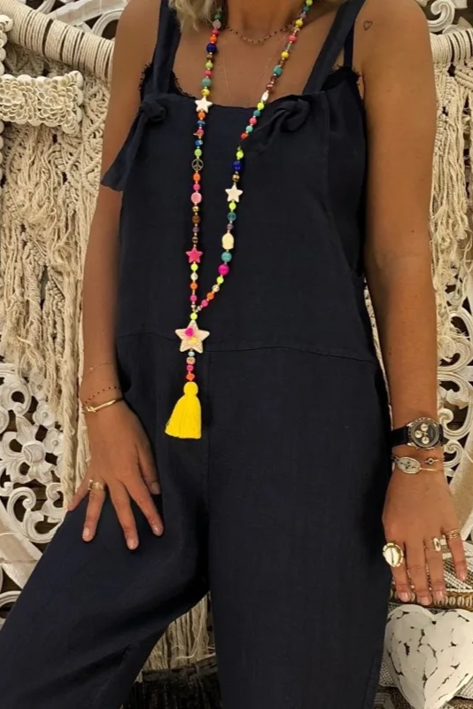 Person wearing a navy jumpsuit with colorful jewelry against an ornate stone wall.