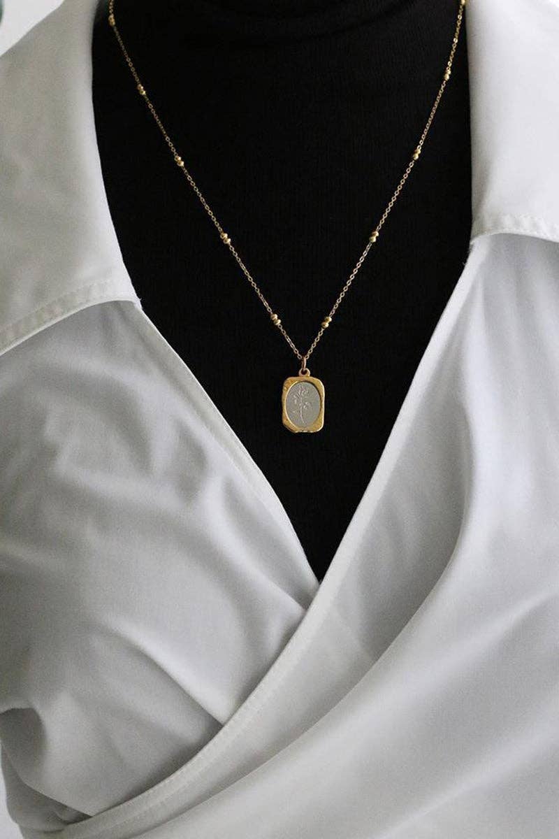 Gold necklace with a pendant on a black background, worn by a person in a light gray shirt.