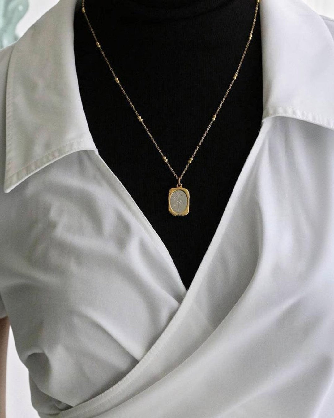 Gold necklace with a pendant on a black background, worn by a person in a light gray shirt.