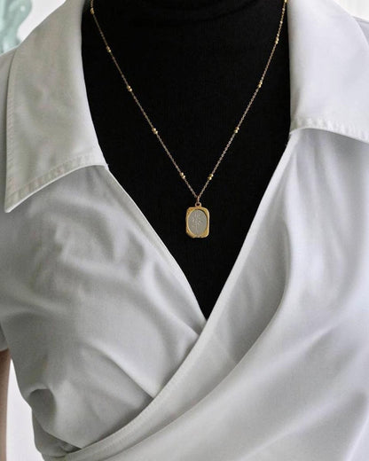 Gold necklace with a pendant on a black background, worn by a person in a light gray shirt.