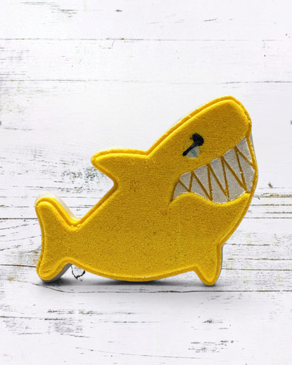 Calla Lily Cosmetics + CL kids yellow shark-shaped bath bomb with pineapple scent on a white wooden background
