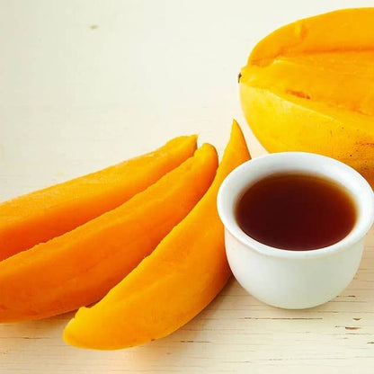 Mango slices and a small bowl of dark liquid on a light background