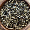 Dry tea leaves in a wooden bowl on a wooden surface