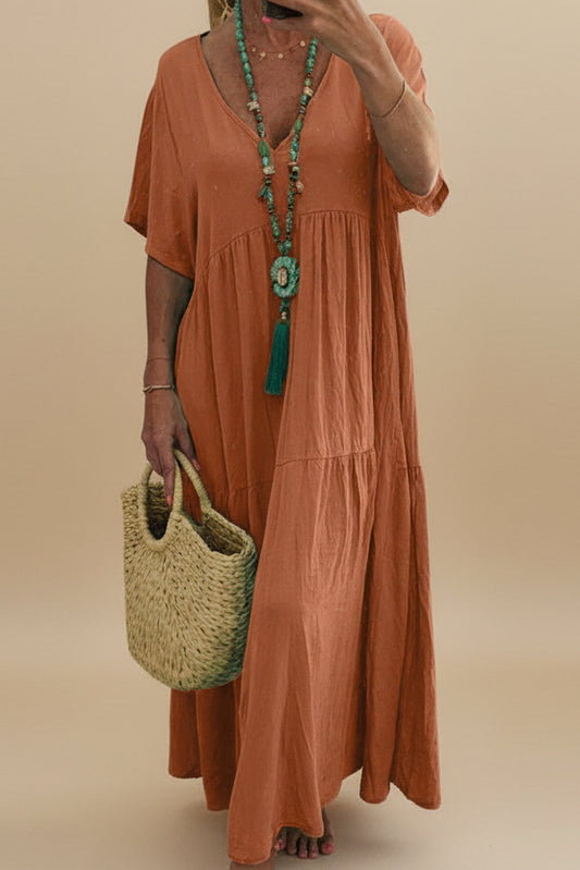 Woman in an orange dress holding a straw bag with a plant and pink bag in the background