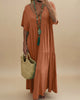 Woman in an orange dress holding a straw bag with a plant and pink bag in the background