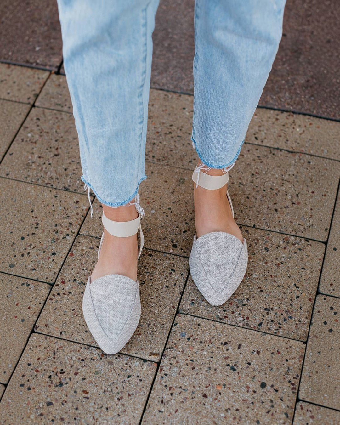 White pointed-toe shoes worn with light blue jeans on a tiled floor.