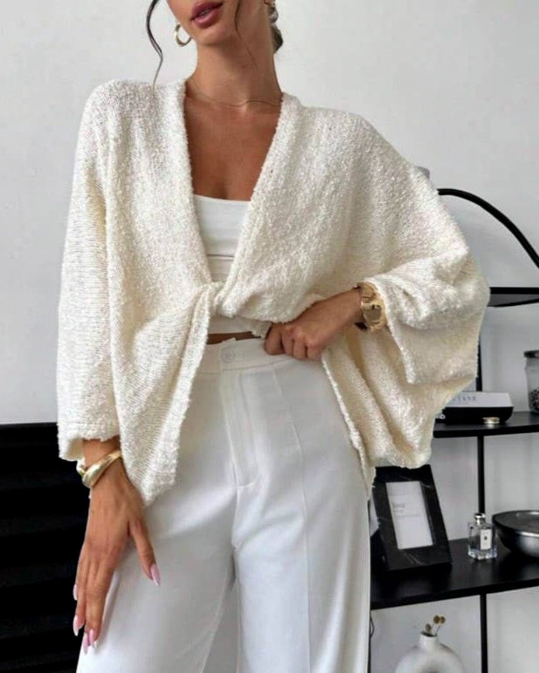 Woman wearing a white textured cardigan over a white top and pants in an indoor setting.