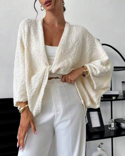 Woman wearing a white textured cardigan over a white top and pants in an indoor setting.