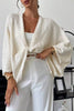 Woman wearing a white textured cardigan over a white top and pants in an indoor setting.