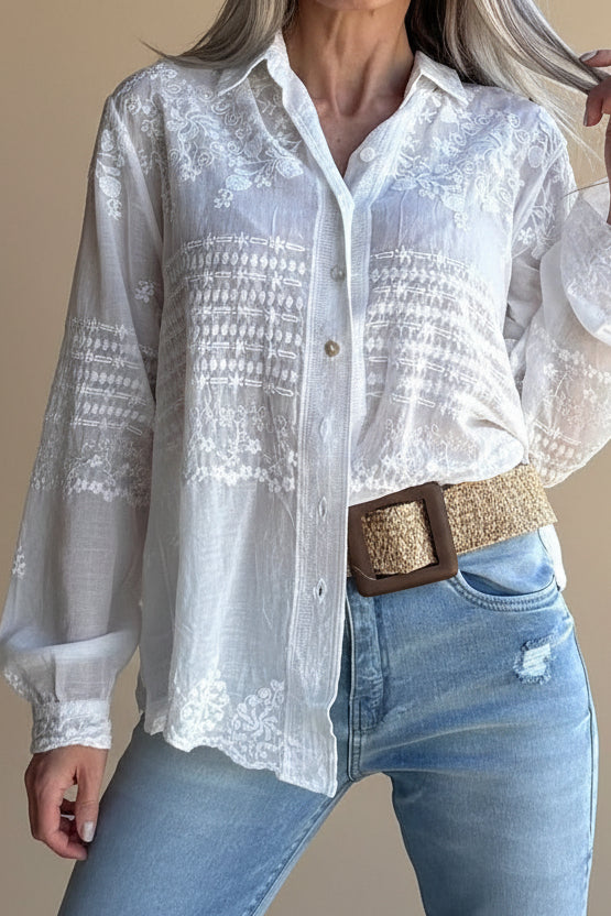 Person wearing a white embroidered blouse and blue jeans with a brown belt.