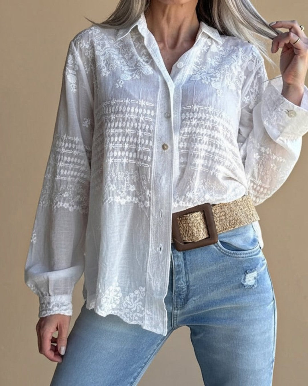 Person wearing a white embroidered blouse and blue jeans with a brown belt.