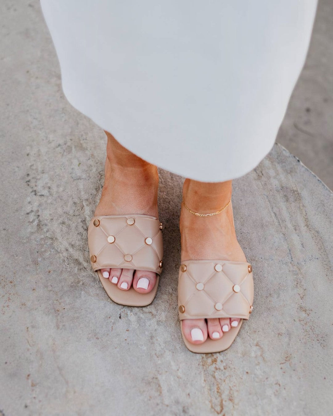 Beige sandals with pearl embellishments worn by a person on a light stone surface.