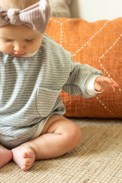 Baby in a striped outfit sitting on a textured surface with an orange cushion in the background