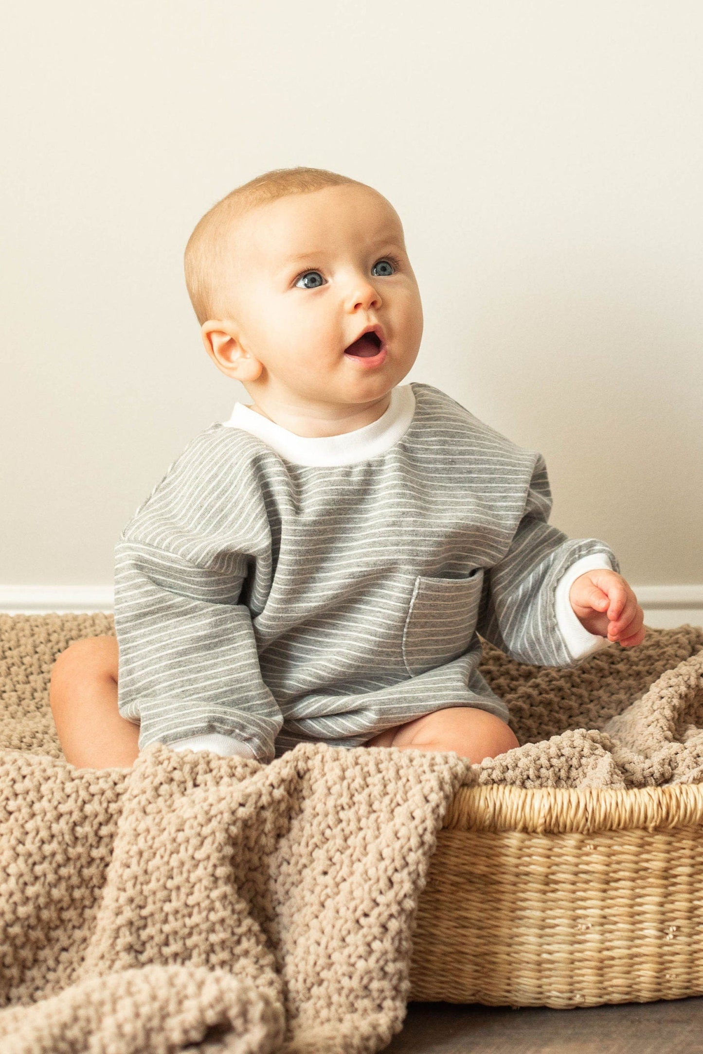 Baby sitting in a woven basket with a textured blanket on a neutral background