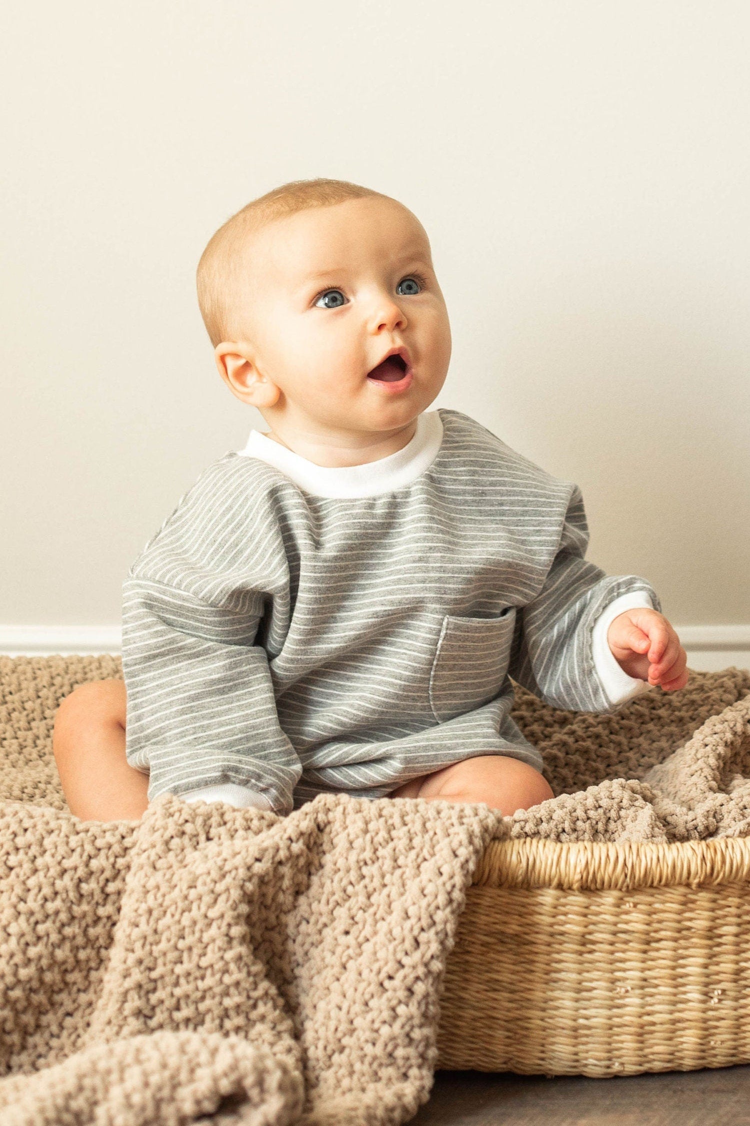 Baby sitting in a woven basket with a textured blanket on a neutral background
