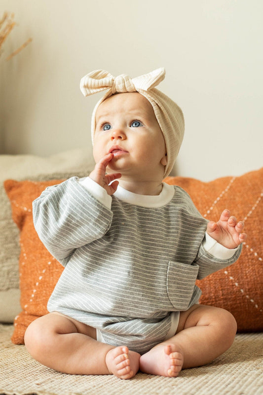 Baby sitting on a couch with a bow headband, surrounded by cozy pillows and decor.