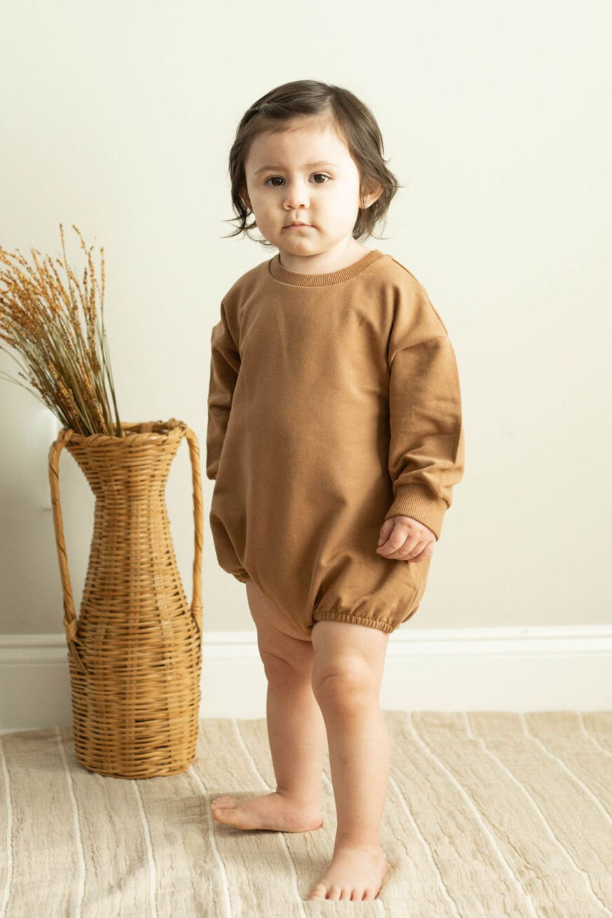 Child wearing a brown outfit standing next to a woven basket indoors.