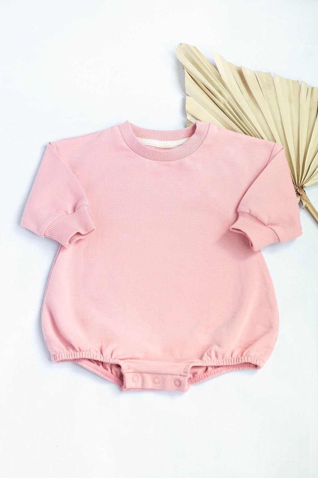 Pink baby romper on a white background with a beige fan