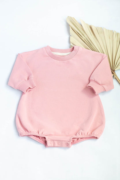 Pink baby romper on a white background with a beige fan