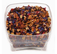 A clear square plastic container filled with loose-leaf herbal tea blend, featuring dried flowers and botanical pieces in orange, brown, purple, and red tones, shown against a plain white background.