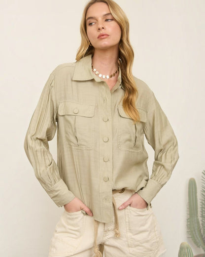 Woman wearing a beige jacket and shorts standing against a plain background with a cactus plant.