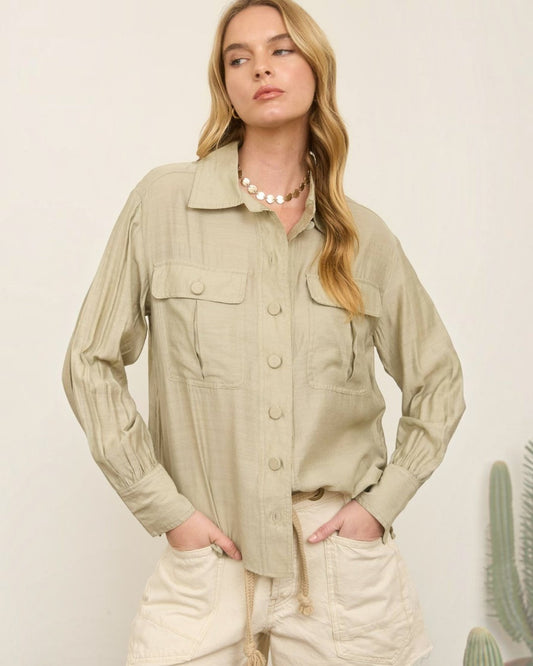 Woman wearing a beige jacket and shorts standing against a plain background with a cactus plant.