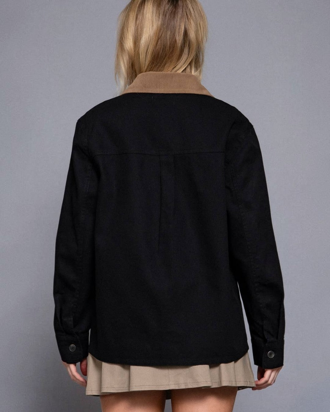 Person wearing a black jacket over a brown shirt with a gray background