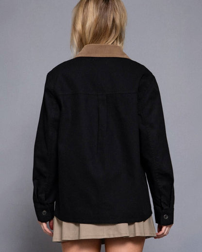 Person wearing a black jacket over a brown shirt with a gray background